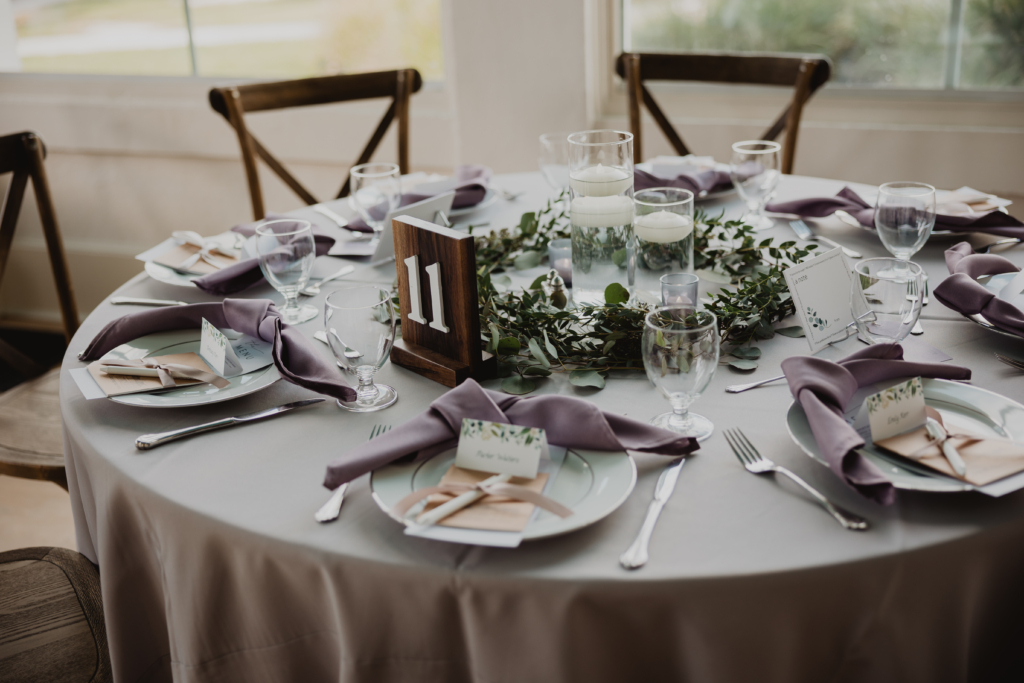 Table scape consisting of floating candle, greenery, rustic table number and wedding color mauve.