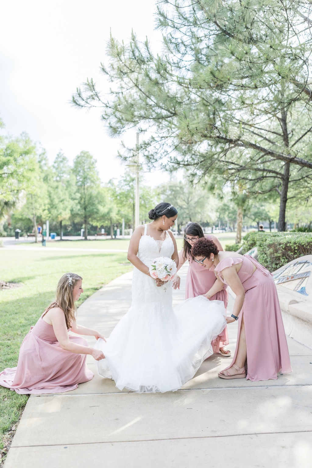 bridesmaids in pink gowns helping bride with her train