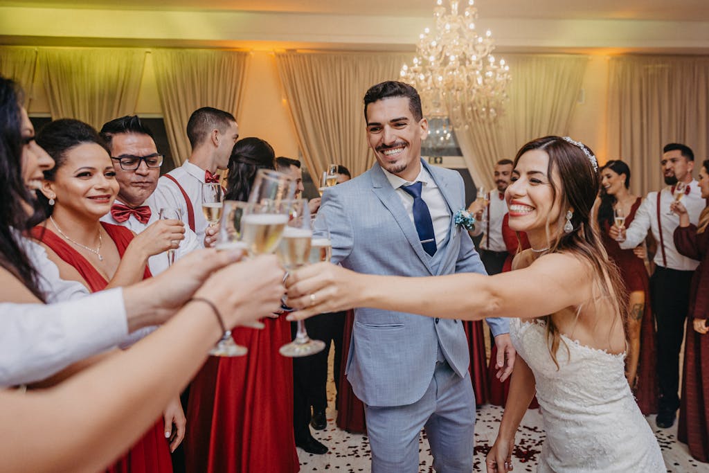 A joyful bride and groom toast with guests in a lively wedding celebration indoors.